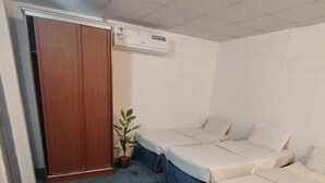 A room with two beds, a wardrobe, a potted plant, and an air conditioning unit. - Al Awali Economic Apartments (Madinah)