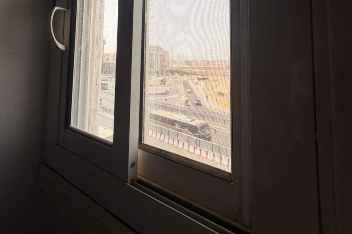 A room with two windows, one with a view of a cityscape and the other with a view of a building.