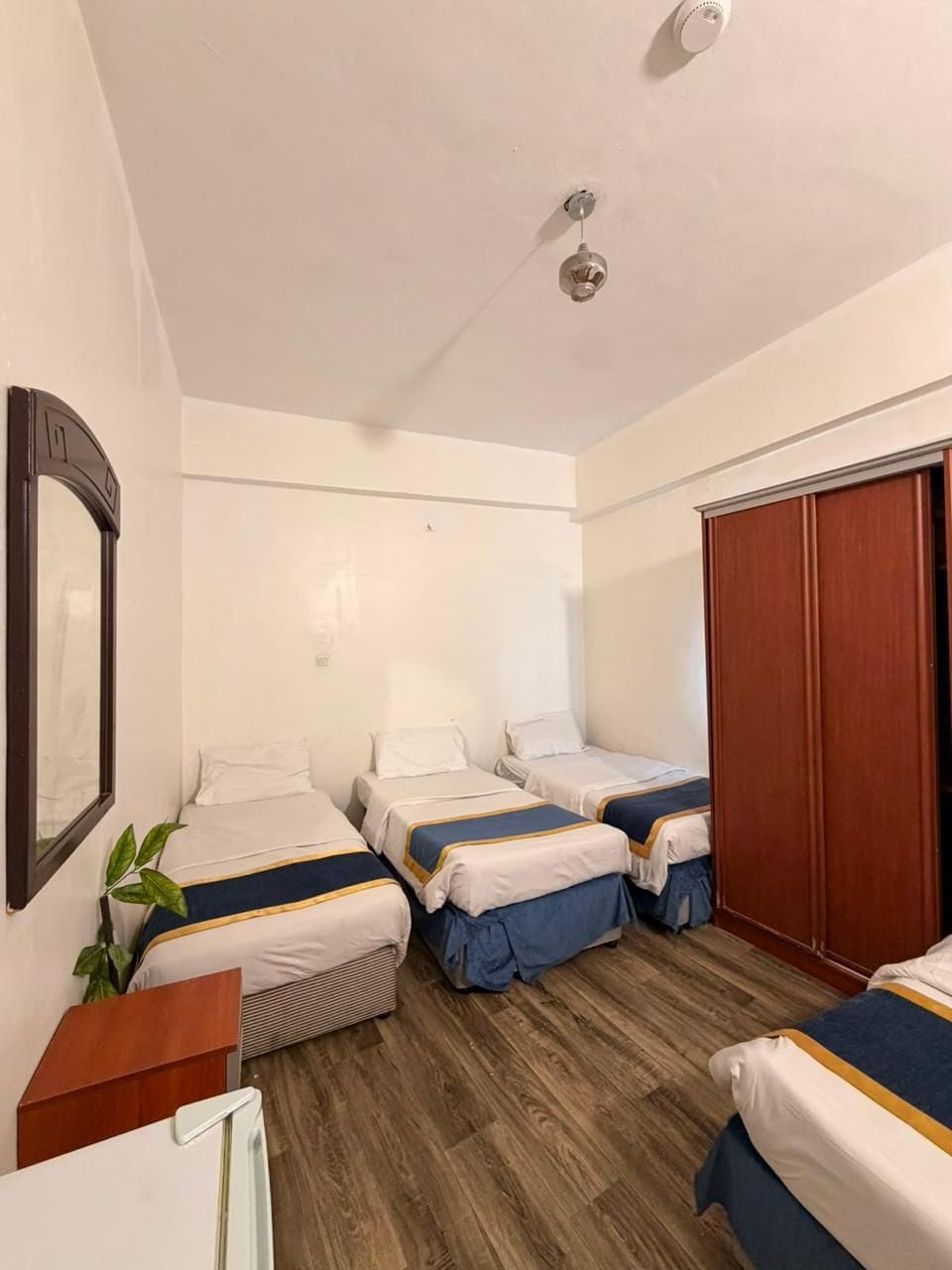 A hotel room with two single beds, a wooden wardrobe, a mirror, and a small table.