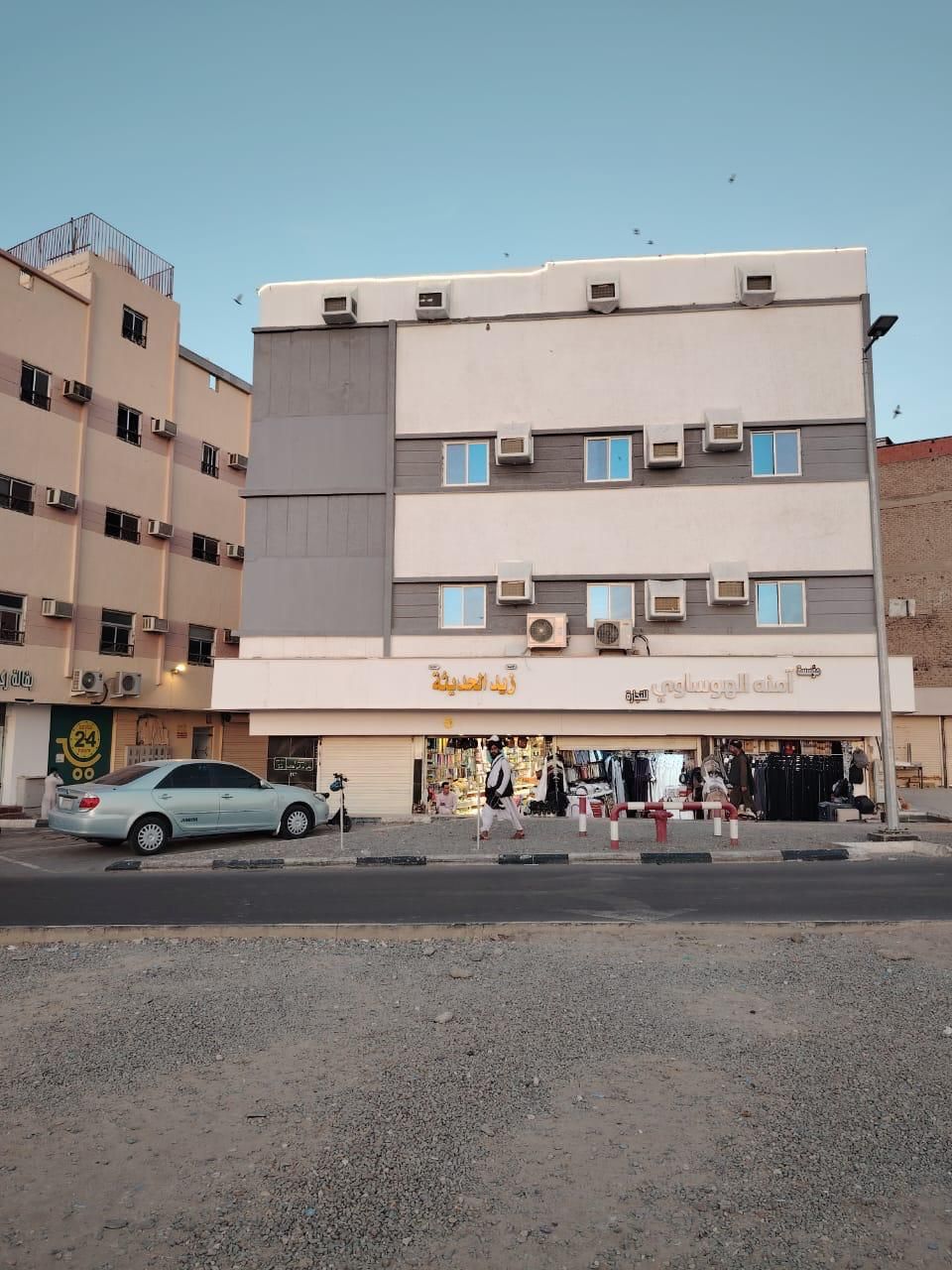 Un immeuble à plusieurs étages avec un commerce au rez-de-chaussée et une voiture garée.
