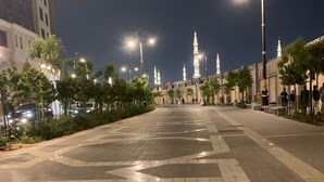 A spacious plaza with tiled flooring, street lamps, and a mosque with illuminated minarets in the background. - Al Awali Economic Apartments (Madinah)