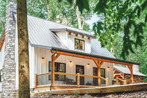 A two-story house with a stone chimney, a covered porch, and a metal roof. - Chapter's End Luxury Retreat (Logan)