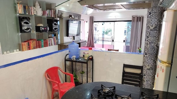 Una cocina compacta con estufa a gas, una silla de plástico roja y un dispensador de agua.