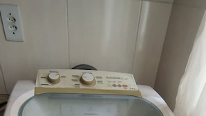 Una lavadora compacta con puerta de vidrio, ubicada sobre un piso de baldosas en una habitación pequeña.