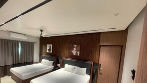 A hotel room with two beds, a ceiling fan, a wooden wall panel, and a door. - KB MARINA PARK (Chennai)