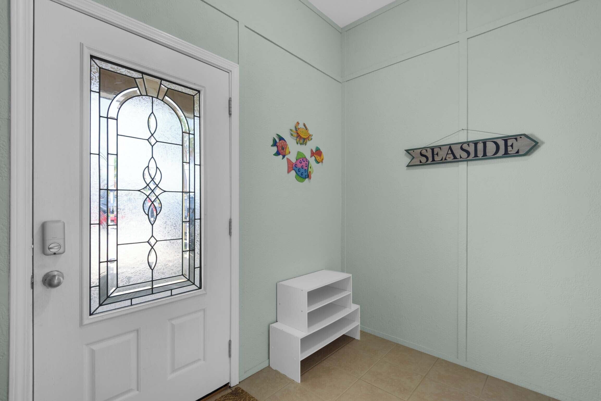 A white door with a glass panel, a small white bench, and a 'SEASIDE' sign on the wall.