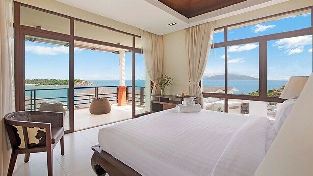 A spacious bedroom with a large bed, a seating area, and a balcony with a view of the sea.