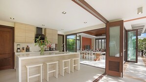 A modern kitchen with a central island, white bar stools, and a dining area with a glass door leading outside.