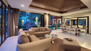 A spacious living area with a large sofa, a glass coffee table, and a dining area with white chairs and a table.