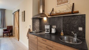A modern kitchen with a black countertop, stainless steel sink, and a coffee maker. There is a wooden chair and a sliding door in the background. - Ground Floor Romantic Apt in Valkenburg (Valkenburg aan de Geul)