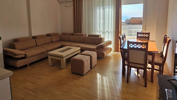 A living room with a sectional sofa, a coffee table, and a dining area with a table and chairs. - Albania Dream Saranda Apartments (Sarandë)