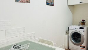 Ein kleiner, sauberer Raum mit Tisch, Stühlen, einer Waschmaschine und an der Wand befestigten Blumentöpfen.