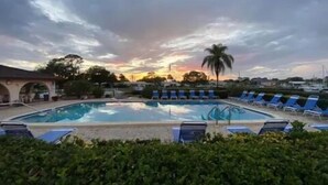 Una piscina con sillas de descanso, rodeada de vegetación y un edificio con arcos.