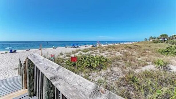 Una playa con un paseo marítimo de madera que conduce a la orilla, arena y vista al océano.