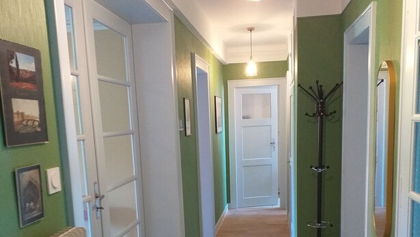 A hallway with green walls, white doors, and a wooden floor. There is a coat rack and a hanging light fixture. - "Place Monet", a pretty, tree-lined square in the center of town. (Saverne)