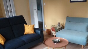 A living room with a dark blue sofa, a light blue sofa, a small round table, and a patterned rug. - "Place Monet", a pretty, tree-lined square in the center of town. (Saverne)