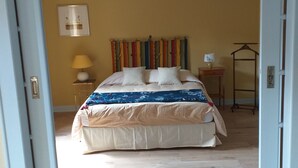 A bedroom with a bed, a bedside table, a lamp, a hanging coat rack, and a patterned rug. - "Place Monet", a pretty, tree-lined square in the center of town. (Saverne)