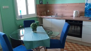 A compact kitchen with a dining area, featuring a round glass table, blue chairs, a small potted plant, and a checkered floor. - "Place Monet", a pretty, tree-lined square in the center of town. (Saverne)