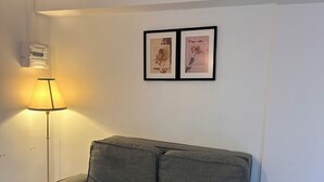 Un canapé gris avec deux coussins, dans une pièce aux murs blancs, avec une lampe et deux tableaux encadrés accrochés au mur.