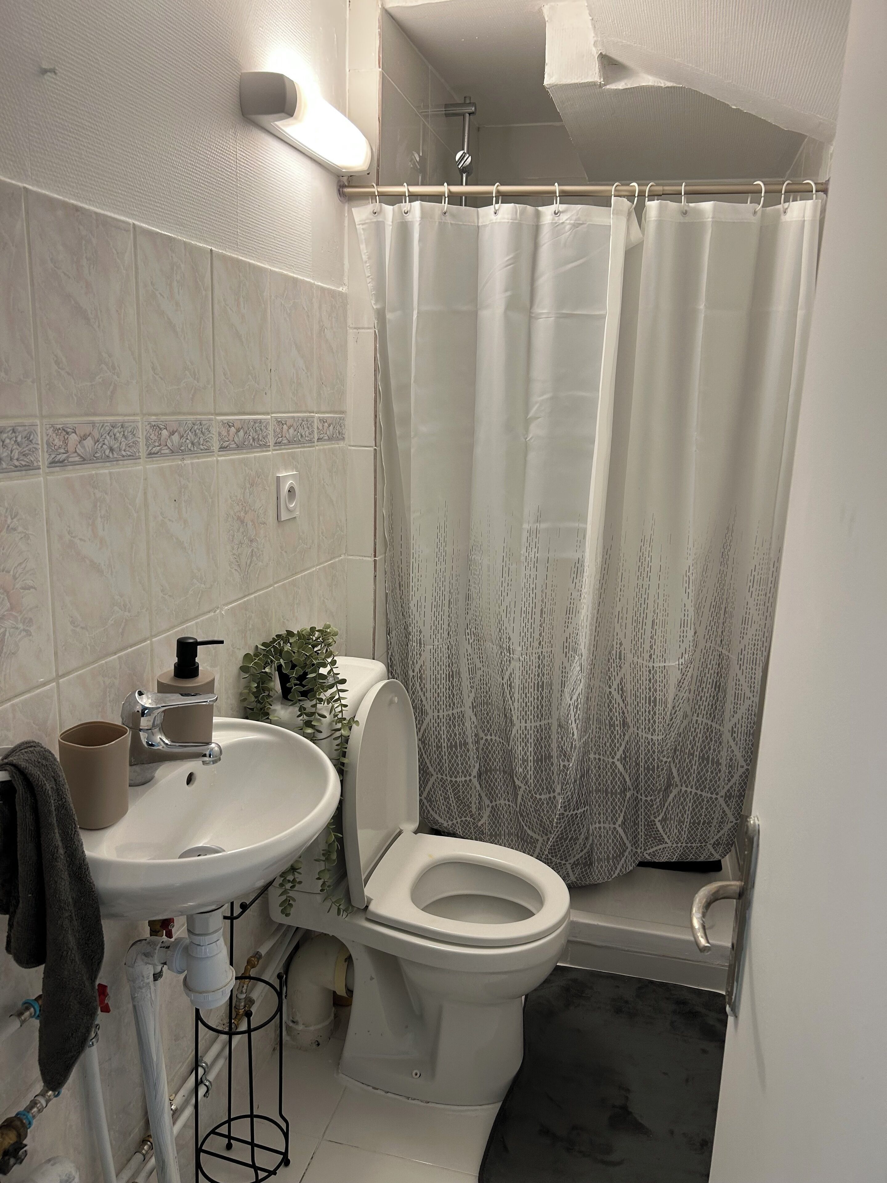A bathroom with a toilet, sink, shower curtain, and a towel hanging on the wall.
