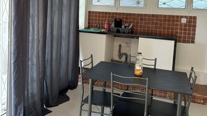 Un espace repas avec une table et des chaises, un coin cuisine avec un mur recouvert de carreaux, et une fenêtre donnant sur un paysage agréable.