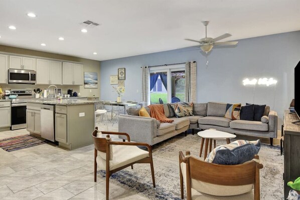 A modern kitchen with stainless steel appliances, a dining area with a glass table, and a living room with a gray sofa and wooden chairs. - OCEAN VIEW | 6 bedrooms, 2 Game rooms, Parking, AC (Daytona Beach Shores)