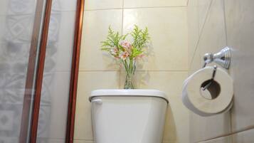 Un baño con inodoro, baldosas de suelo estampadas, un florero y un dispensador de papel higiénico.