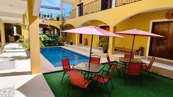 Zona de piscina con mesa y sillas, rodeada de paredes amarillas y un balcón.