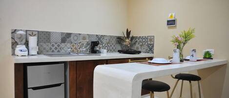 A compact kitchen with a built-in refrigerator, a coffee maker, and a sink. There are two stools at the counter.