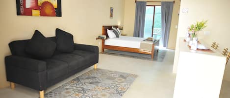 Una habitación de hotel moderna con un sofá negro, una cama con cabecera de madera, una alfombra estampada y vistas al exterior a través de un ventanal grande.