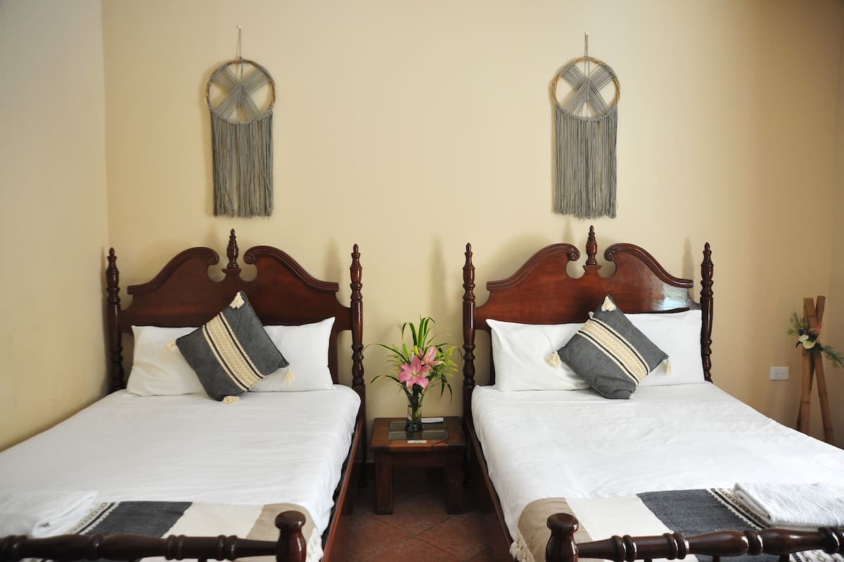 A double bed with a wooden headboard, a bedside table with a vase of flowers, and a wall-mounted macrame decoration.
