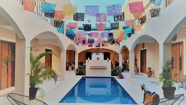 Un cortile con piscina, circondato da archi e decorato con sagome di carta colorate.