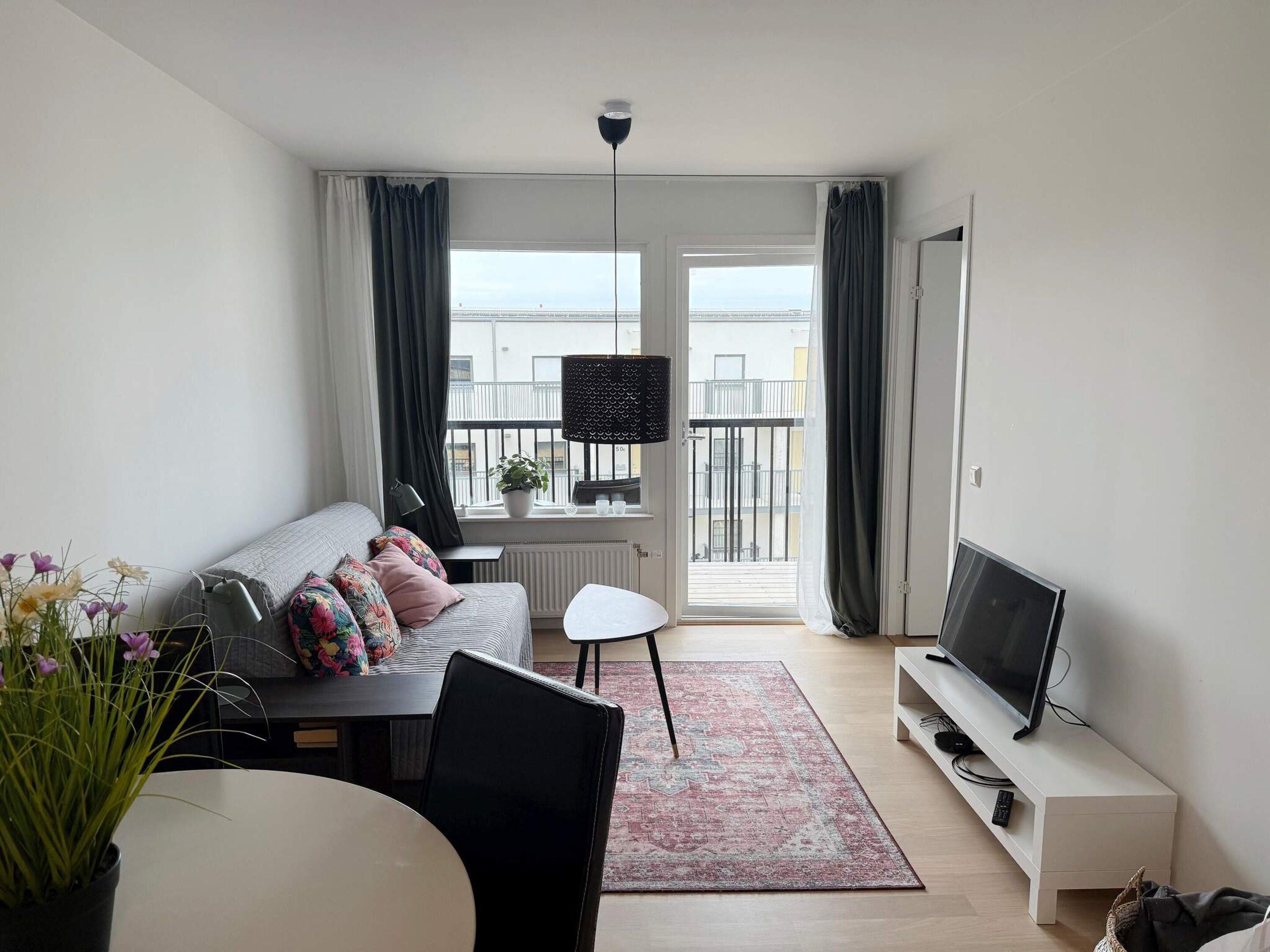 A modern living room with a sofa, a dining table, a TV, and a balcony with a view.