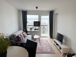 Een moderne woonkamer met een bank, een eettafel, een televisie en een balkon met uitzicht.