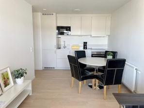 A modern kitchen with white cabinets, a microwave, and a coffee machine. There is a round table with black chairs and a potted plant. - 4 Star Holiday Home in Visby (Visby)