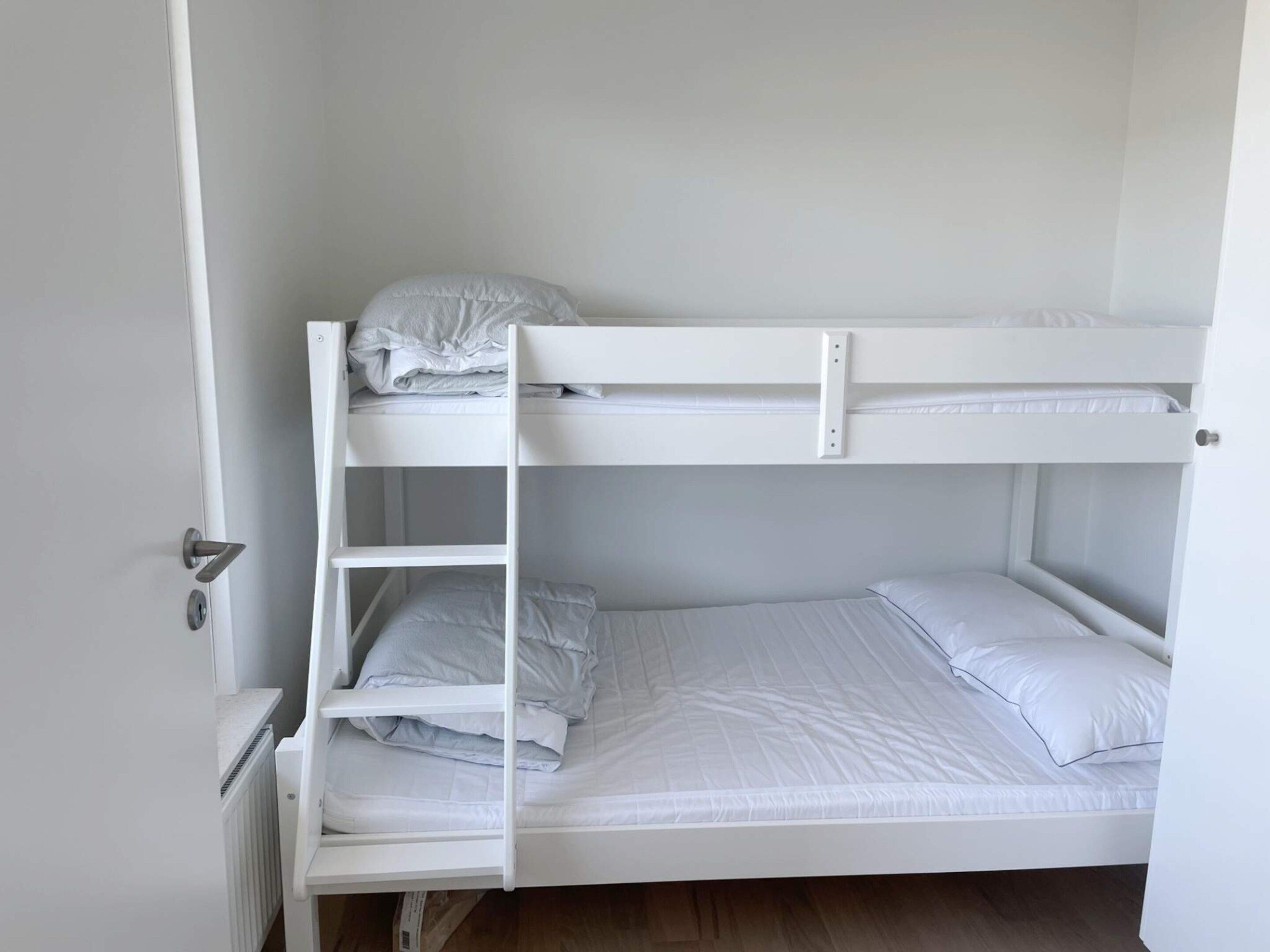 Een stapelbed met een ladder, witte beddengoed en een deur met een handvat.