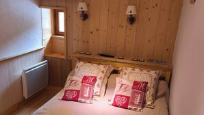 A bedroom with a wooden headboard, a window, a radiator, and two wall-mounted lamps.
