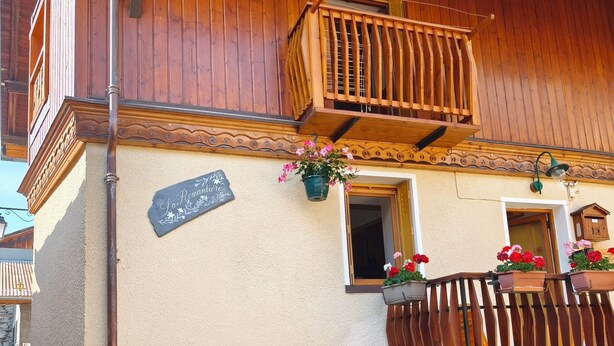 A traditional wooden building with a balcony, a stone base, and flower pots.