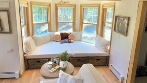 A cozy room with a large window seat, wooden beams on the ceiling, and a framed bear picture on the wall.