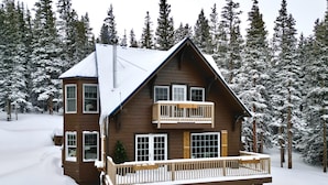 A two-story log cabin with a balcony, surrounded by snow-covered trees.