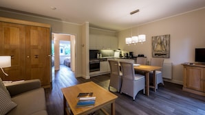 A modern kitchen with white cabinets, a dining area with wicker chairs, a wooden table, and a television on a wooden cabinet. - Ferienwohnung fur Zwei Personen, Dierhagen (Ostseebad Dierhagen)