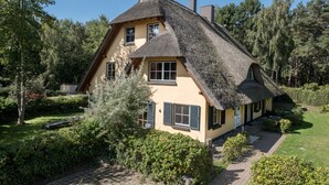 A traditional house with a steep thatched roof, surrounded by lush greenery and trees. - Ferienwohnung fur Zwei Personen, Dierhagen (Ostseebad Dierhagen)