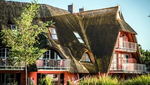 A house with a unique curved roof and a balcony with a railing. - Ferienwohnung fur Zwei Personen, Dierhagen (Ostseebad Dierhagen)