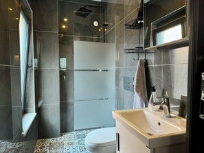 Un baño moderno con cabina de ducha de vidrio, inodoro blanco y lavamanos con espejo.