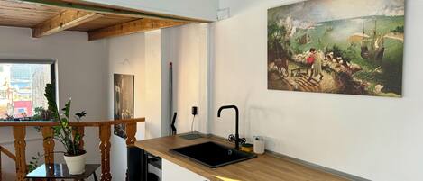 A kitchen with a wooden countertop, black sink, and a painting of a landscape on the wall.