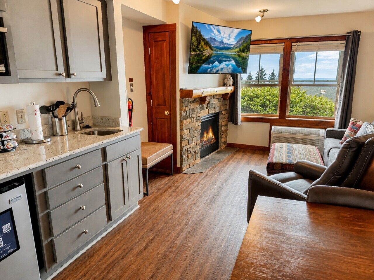 A modern kitchen with a stone fireplace, a dining area with a sofa, and a large window with a view.