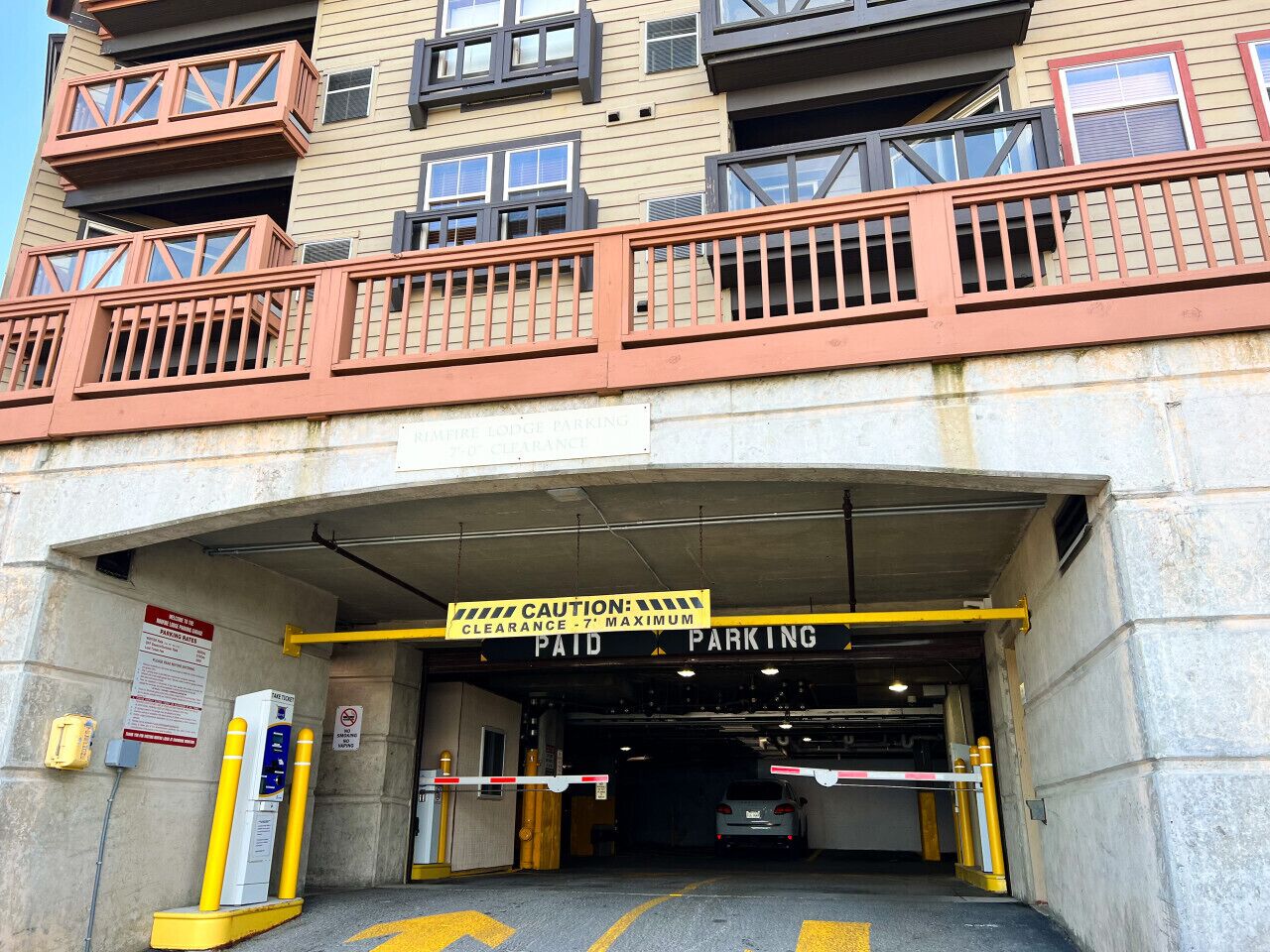 L’entrée d’un parking payant, avec un panneau d’avertissement, une barrière jaune et une voiture à l’intérieur.