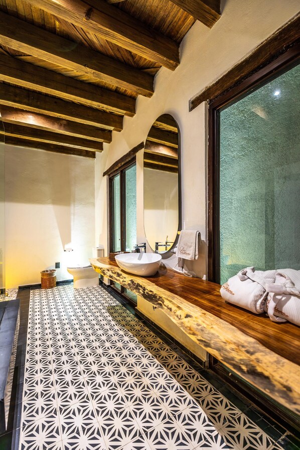 A bathroom with a wooden ceiling, a large mirror, a sink, and patterned floor tiles. - Hotel Palacio Del Gambusino (Real de Catorce)