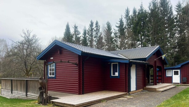 En rød hytte med blå tag, træterrasse og en lille veranda.
