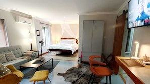 Moderni hotellihuone, jossa on sänky, sohva, tuoli, työpöytä ja televisio.